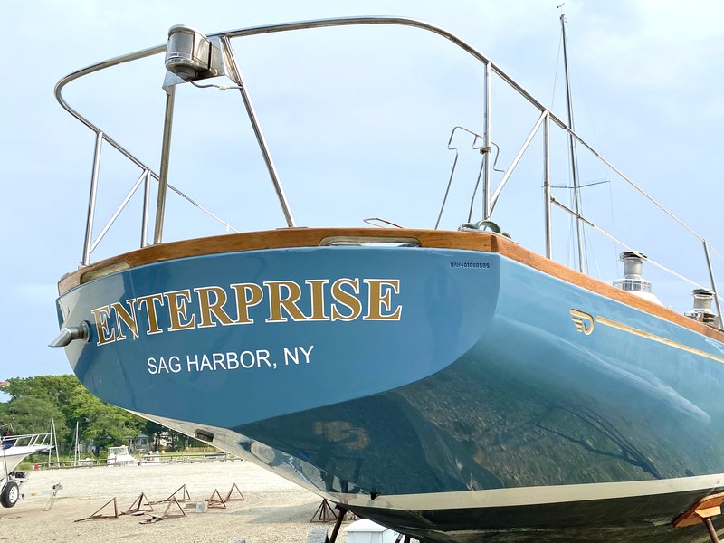Gold serif boat lettering reading ENTERPRISE with SAG HARBOR NY hailing port on a blue sailboat hull