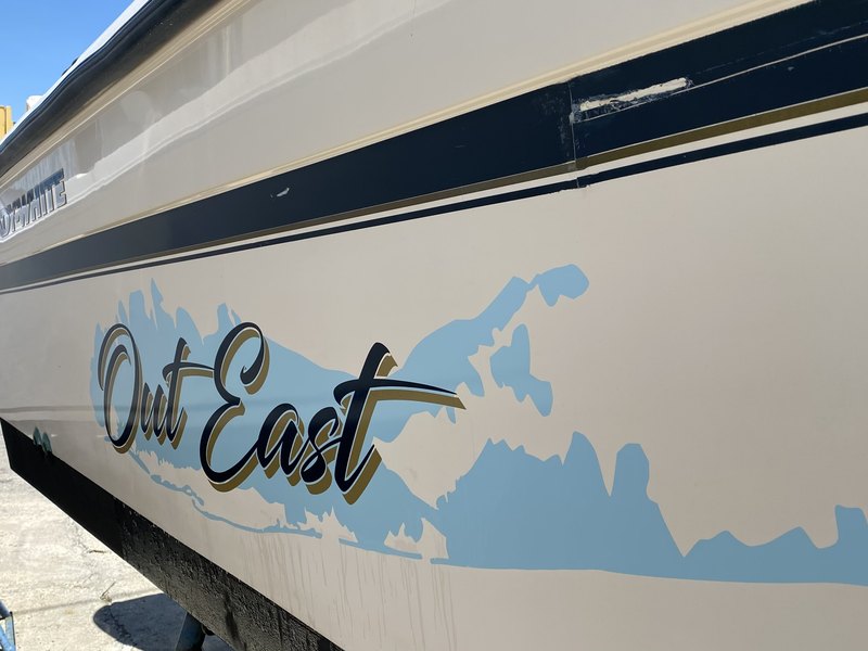 Navy and gold script boat lettering reading Out East on a Grady-White hull with a light blue Long Island silhouette graphic