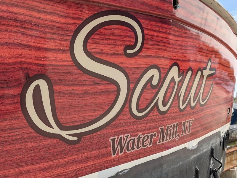 Cream and brown script boat lettering reading Scout with Water Mill NY hailing port on a red wood-grain hull
